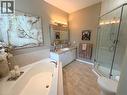 Corner soaking tub, glass-enclosed shower, single vanity with light-colored countertop, wall-mounted light fixture, and tiled flooring - 40 Stornoway Crescent, Huron East, ON 