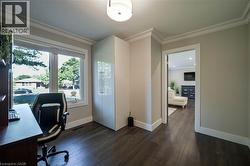 Room featuring dark wood-finish flooring, crown molding, a large window, and a built-in white high-gloss cabinet - 