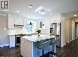 Kitchen featuring a center island with waterfall countertop, stainless steel appliances, white cabinetry, and wood-finish flooring - 