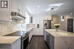 Kitchen featuring white shaker cabinetry, stainless steel appliances, stone slab countertops, wood-finish flooring, and pendant lighting - 