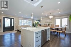 Open-concept living area with dark wood-finish flooring, recessed lighting, a large kitchen island with a waterfall countertop, and a double entry door with frosted glass panels - 