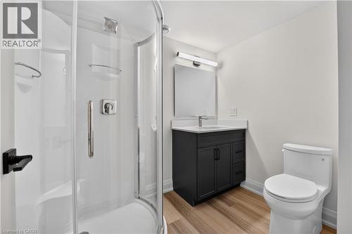 Glass-enclosed shower with chrome fixtures, dark wood-finish vanity with an integrated sink, wall-mounted mirror, and wood-finish flooring - 8905 Angie Drive, Niagara Falls, ON 