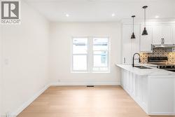 Modern kitchen featuring white shaker cabinetry, an integrated sink, a dark faucet, patterned tile backsplash, and light wood-finish flooring - 