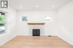 White brick fireplace with a wood mantel, light wood-finish flooring, recessed lighting, and multiple windows - 
