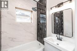 Tiled shower surround with a window, dark-toned wall tile, shower system with a rain shower head, rectangular vanity mirror, and a vanity with an integrated sink - 