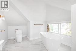 Freestanding soaking tub with a floor-mounted gold-finish faucet, large window, and marbled-finish tile flooring - 