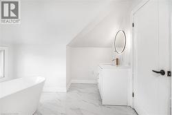 White freestanding soaking tub, single vanity with a white countertop, oval illuminated mirror, and marble-look tile flooring - 