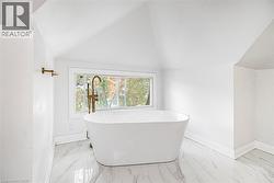 Freestanding soaking tub with floor-mounted brass faucet, marble-finish tile flooring, and sloped ceiling - 