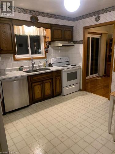 Wood-finish cabinetry, white tile backsplash, a stainless steel dishwasher, a white range, and a dual basin sink - 410 Lakeview Drive, Waterloo, ON 