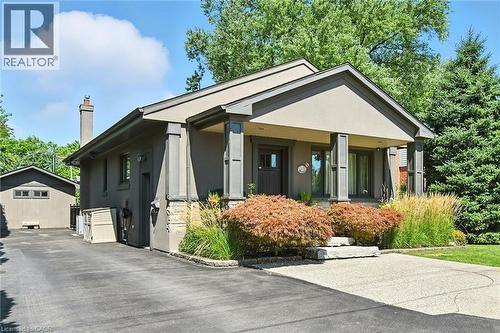 Paved driveway leading to a stucco exterior with stone accents, a covered front porch, and mature landscaping - 2209 Ghent Avenue, Burlington, ON 
