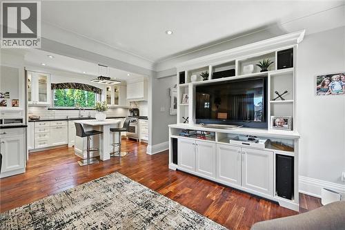 Hardwood-finish flooring, built-in entertainment center with integrated shelving, white cabinetry, recessed lighting, and a kitchen island with seating - 2209 Ghent Avenue, Burlington, ON 
