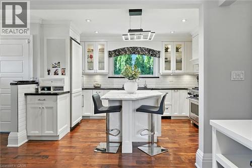 White cabinetry with glass-front accents, dark countertops, a subway tile backsplash, and wood-finish flooring - 2209 Ghent Avenue, Burlington, ON 