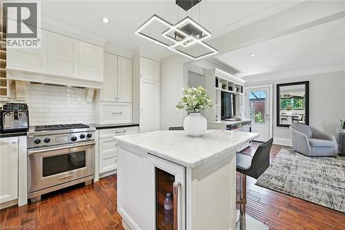 Kitchen featuring white shaker-style cabinetry, a stainless steel range with a tile backsplash, wood-finish flooring, a kitchen island with a beverage cooler, and a contemporary ceiling light fixture - 2209 Ghent Avenue, Burlington, ON 