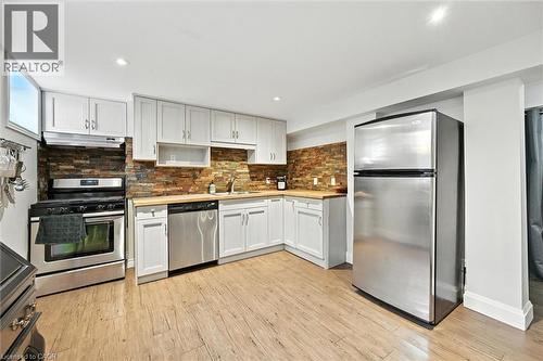 U-shaped kitchen with light wood-finish flooring, white cabinetry, a stone-tile backsplash, stainless steel appliances, and wood-finish countertops - 2209 Ghent Avenue, Burlington, ON 