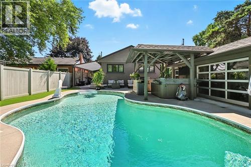 Curved swimming pool, paved pool surround, enclosed spa, wood pergola, and a glass-paneled garage door - 2209 Ghent Avenue, Burlington, ON 