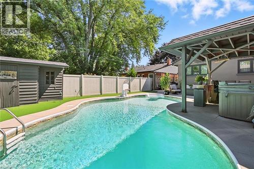 Freeform swimming pool with concrete surround, adjacent covered patio, and a separate storage shed - 2209 Ghent Avenue, Burlington, ON 