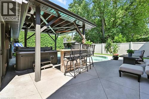 Expansive concrete patio featuring a hot tub, covered pergola, and in-ground swimming pool - 2209 Ghent Avenue, Burlington, ON 
