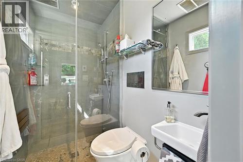Tiled shower enclosure with glass surround, pebble flooring, and a built-in shower bench - 2209 Ghent Avenue, Burlington, ON 