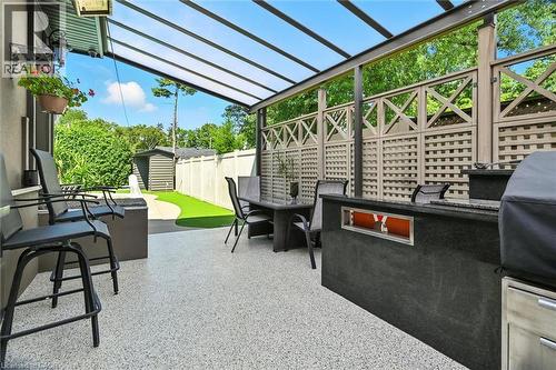 Covered patio with a clear panel roof, textured privacy screening, and a built-in outdoor kitchen island with a stone finish - 2209 Ghent Avenue, Burlington, ON 
