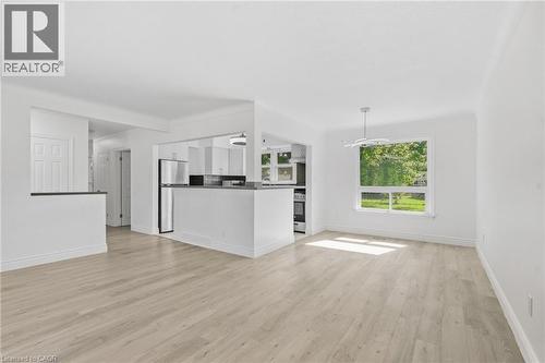 Neutral toned wood-finish flooring throughout, stainless steel appliances, modern overhead lighting fixture, and a large window - 49 Beverly Crescent, Welland, ON 