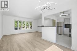 Open concept living space featuring wood-finish flooring, a contemporary chandelier, a bay window, a breakfast bar, and stainless steel appliances - 