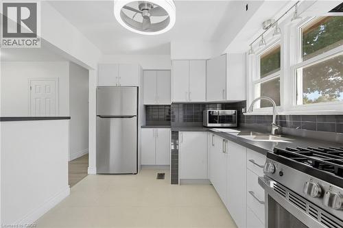Contemporary kitchen featuring white cabinetry, stainless steel appliances, dark gray countertops, and a subway tile backsplash - 49 Beverly Crescent, Welland, ON 