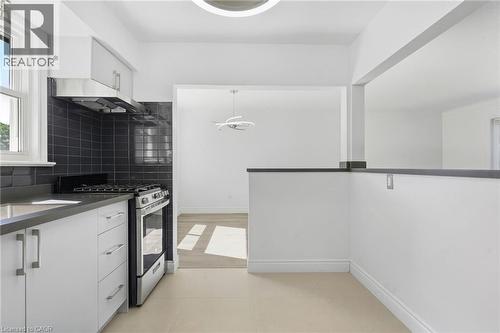 Kitchen featuring white cabinetry, stainless steel appliances, dark subway tile backsplash, and light tile flooring - 49 Beverly Crescent, Welland, ON 