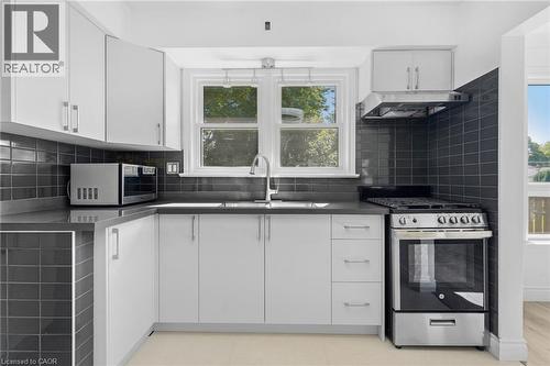 Kitchen featuring white cabinetry, dark subway tile backsplash, solid surface countertops, a stainless steel range, and a stainless steel range hood - 49 Beverly Crescent, Welland, ON 