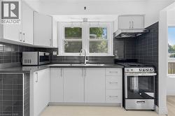 Kitchen featuring white cabinetry, dark subway tile backsplash, solid surface countertops, a stainless steel range, and a stainless steel range hood - 