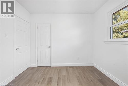 Wood-finish flooring with white trim, white paneled doors, and a white window frame with natural light - 49 Beverly Crescent, Welland, ON 