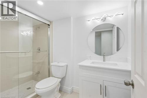 Bathroom featuring a glass-enclosed shower, white vanity with integrated sink, circular mirror, and modern vanity lighting - 49 Beverly Crescent, Welland, ON 
