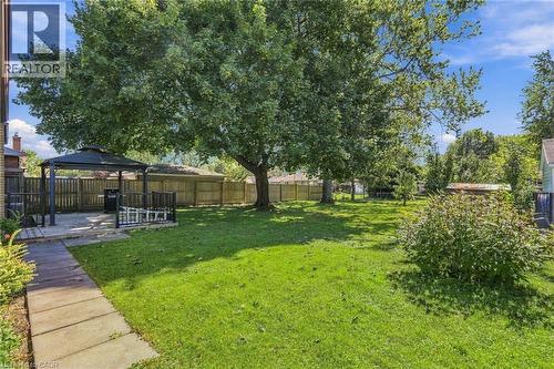Expansive backyard featuring a lush lawn, mature trees, wood fencing, and a concrete paver pathway leading to a patio with a gazebo - 49 Beverly Crescent, Welland, ON 