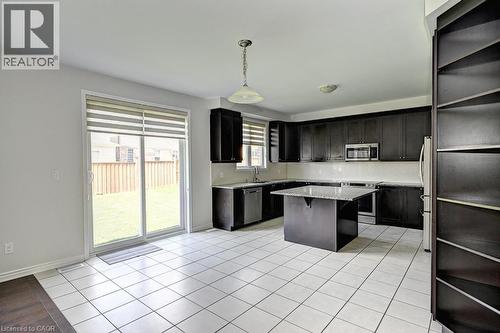 Kitchen with dark wood cabinetry, stainless steel appliances, white tile flooring, and a central island with a light-colored countertop - 236 Ridge Road, Cambridge, ON 