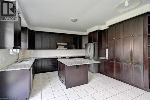 Kitchen featuring extensive dark wood cabinetry, light granite countertops, a central island, and white square tile flooring - 236 Ridge Road, Cambridge, ON 