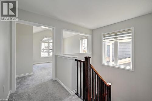 Carpeted hallway with wood staircase, white trim, and interior window feature - 236 Ridge Road, Cambridge, ON 