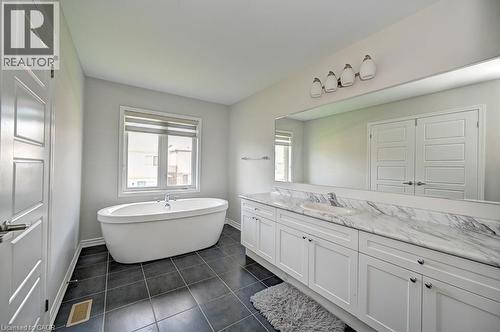 Freestanding soaking tub, dual vanity with undermount sinks, patterned stone countertop, dark tile flooring, and integrated wall mirror - 236 Ridge Road, Cambridge, ON 