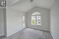 Vaulted ceiling, arched window with horizontal blinds, glass panel door, gray carpeting, and white trim - 