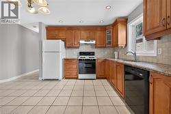 Kitchen featuring tile flooring, wood cabinetry, granite-finish countertops, stainless-steel sink, and a tile backsplash - 