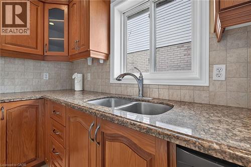 Wood-finish cabinetry, speckled countertop, tile backsplash, stainless steel double basin sink, and an integrated dishwasher - 795 Tenth Avenue, Hamilton, ON 