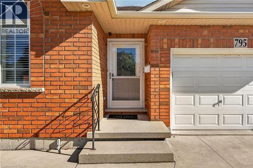 Brick exterior with an arched window, white garage door, concrete steps, and a wrought iron handrail - 795 Tenth Avenue, Hamilton, ON 