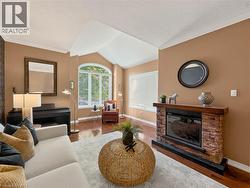 Vaulted ceiling, wood-finish flooring, electric fireplace with stacked stone surround, wood mantel, and large arched window - 