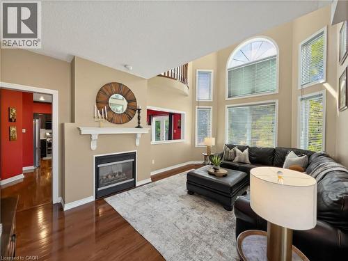 Two-story ceiling, multiple large windows, gas fireplace with mantle, wood-finish flooring, and a second-story interior balcony - 74 Davidson Boulevard, Dundas, ON 