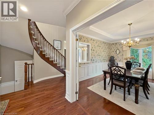 Hardwood-finish flooring, grand curved staircase with wood banister, tray ceiling with crown molding, decorative wainscoting, and a brass chandelier - 74 Davidson Boulevard, Dundas, ON 