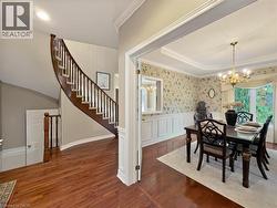 Hardwood-finish flooring, grand curved staircase with wood banister, tray ceiling with crown molding, decorative wainscoting, and a brass chandelier - 