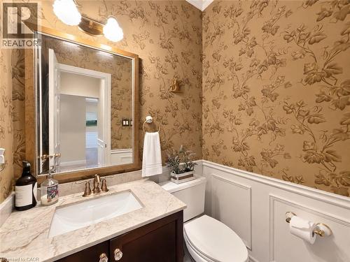 Powder room featuring botanical wallpaper, wainscoting, an undermount sink, a stone-finish countertop, and a wood-finish vanity - 74 Davidson Boulevard, Dundas, ON 