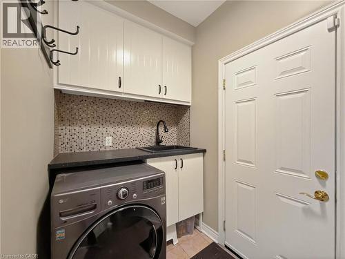 Upper cabinetry, mosaic tile backsplash, integrated utility sink with dark countertop, and paneled entry door - 74 Davidson Boulevard, Dundas, ON 