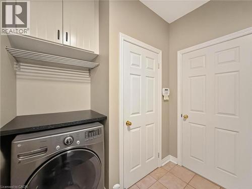 Laundry area featuring overhead cabinetry, a wall-mounted drying rack, a black countertop, and tile flooring - 74 Davidson Boulevard, Dundas, ON 