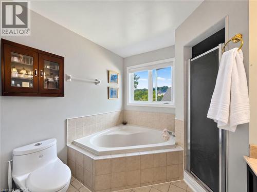 Corner soaking tub with tile surround, walk-in shower with sliding door, wall-mounted wood-finish cabinet with glass doors, and a white toilet - 74 Davidson Boulevard, Dundas, ON 