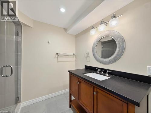 Glass-enclosed shower with tile surround, wood-finish vanity with an undermount sink, dark countertop, and decorative circular mirror - 74 Davidson Boulevard, Dundas, ON 