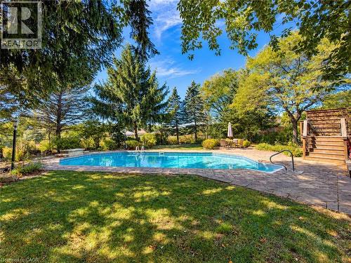 In-ground swimming pool with a stone paver surround, expansive lawn, and mature trees - 74 Davidson Boulevard, Dundas, ON 
